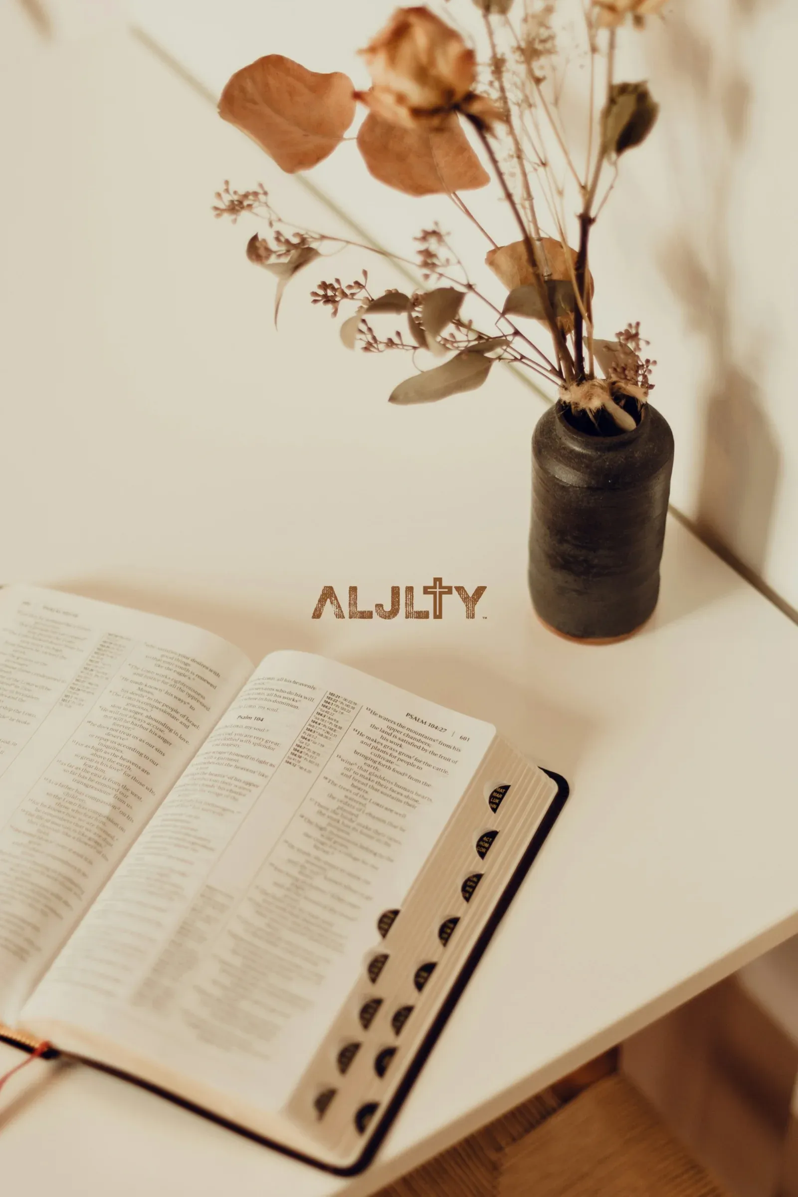 ALJLTY brand wallpaper with copper logo over an open Bible and dried flowers