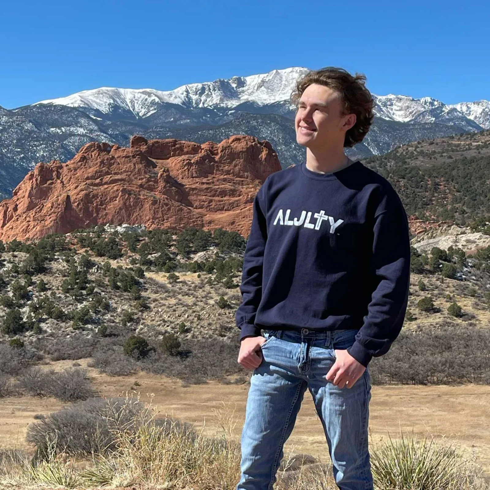 Brenton at Garden of the Gods wearing a navy ALJLTY sweater, with Pikes Peak and red rock formations behind him