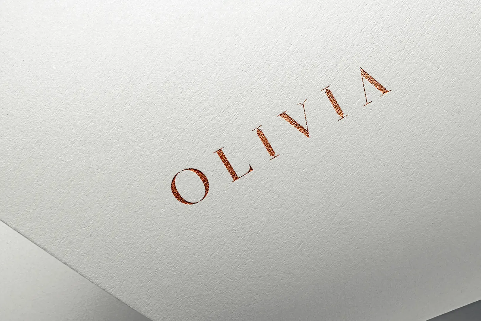 Olivia logo foil-stamped in copper on white cotton paper, showing the custom serif wordmark with generous letter spacing
