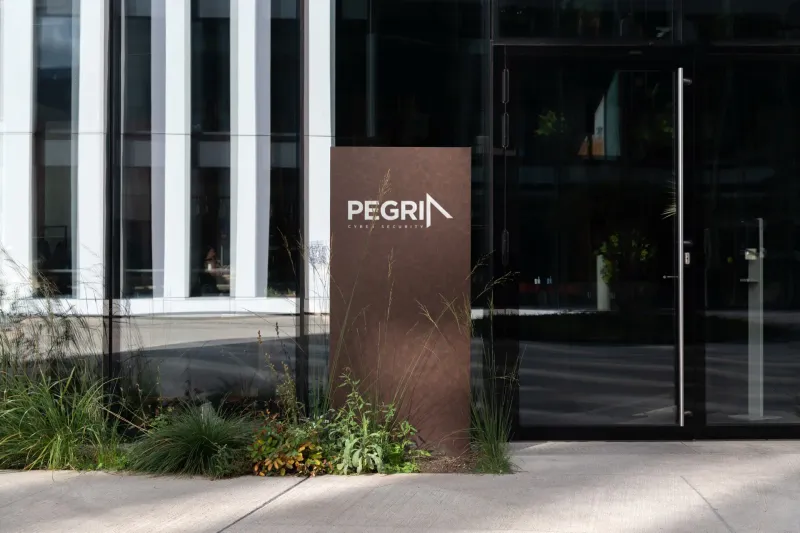 Pegria Cyber Security wordmark on a rust-brown monolith sign outside a modern glass office entrance